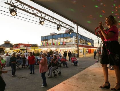 Female singer wearing a pink top and black skirt performing in front of a crowd on a stage across from Joe's Playland by the beach in Salisbury MA