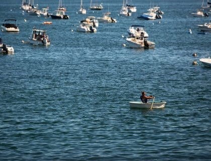 Woman with sunglasses canoeing by boats and moorings in the middle of the blue water in Swampscott MA