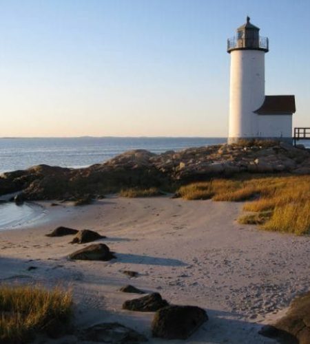 Landscape view of the Annisquam Lighthouse by the beach on a clear day at sunset.