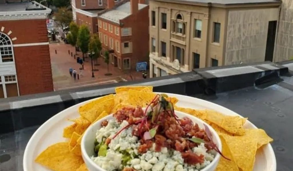 A full plate of tortilla chips with a bowl of guacamole dip in the center on a ledge overlooking the town of Salem MA.